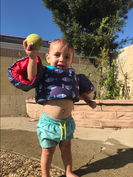 Toddler boy in swim trunks throwing tennis ball in pool
