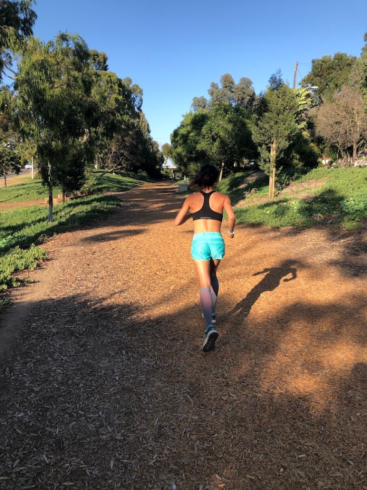 Female runner running in sports bra on running trail.