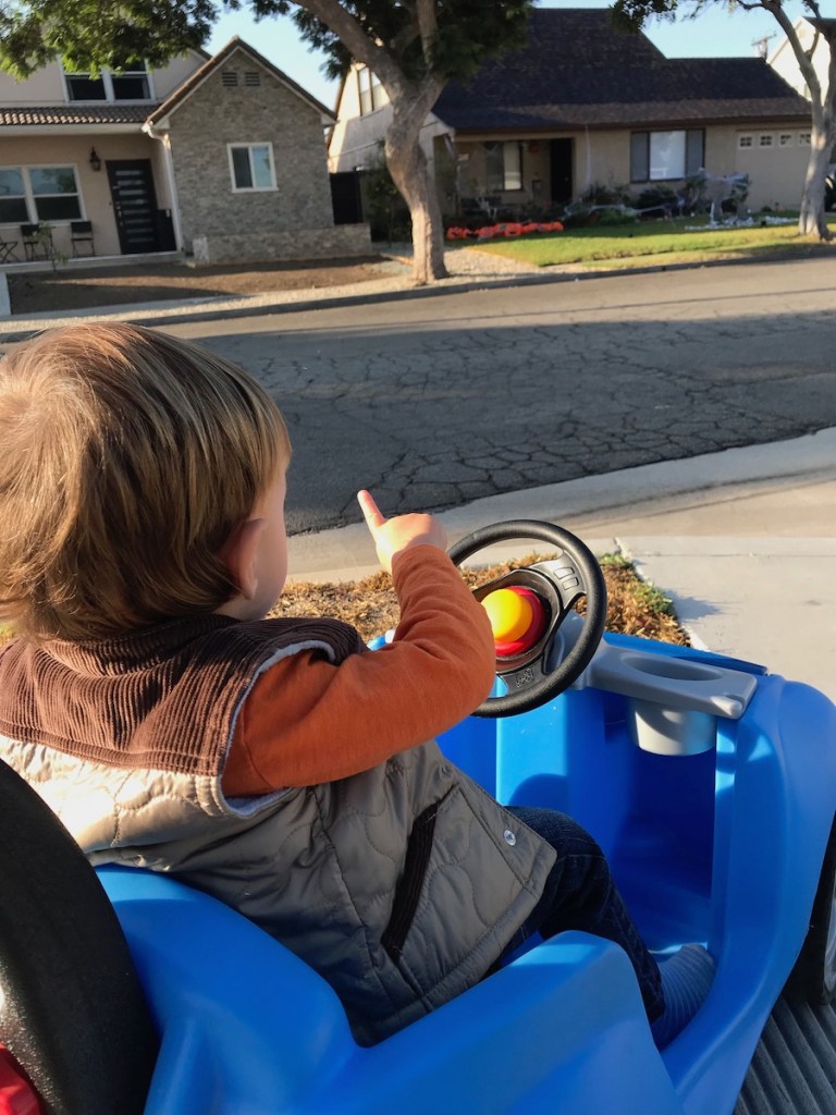 toddler boy in blue push car pointing out to Halloween decorations on a house