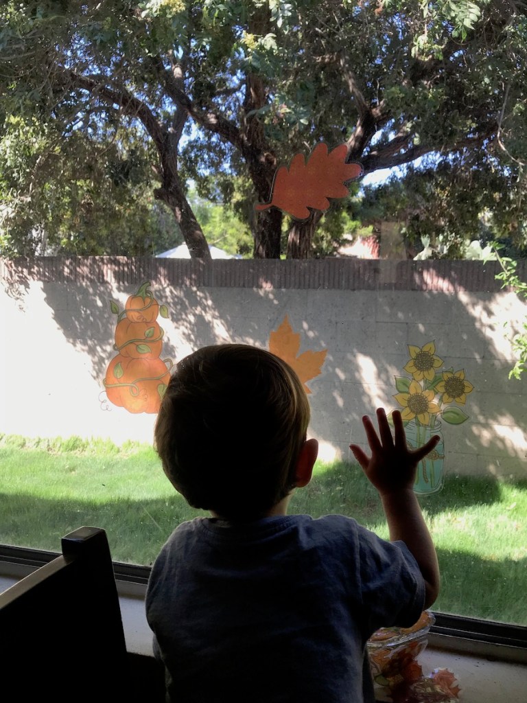 toddler boy decorating window with fall window stickers